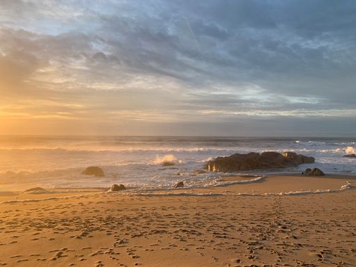 A beautiful landscape of sandy beach and rock formations against blue cloudy sky at sunrise