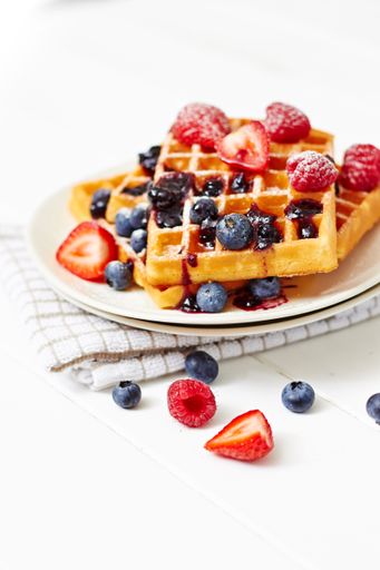 A close-up shot of waffles with syrup and berries in white plate on table napkin isolated on white background