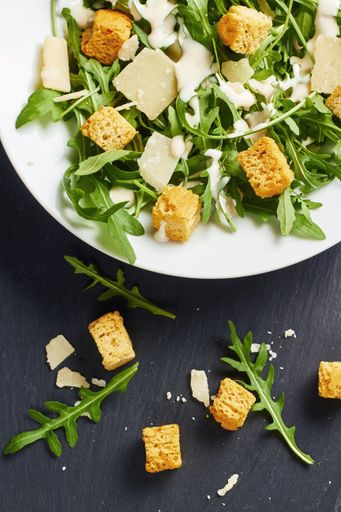 A top view of rucola salad with parmesan cheese and croutons in white plate on a wooden dark blue table
