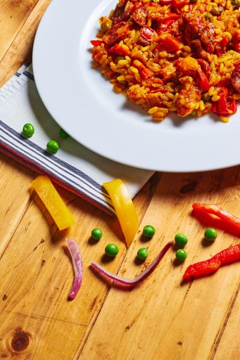 A close-up top view of vegetable paella in white plate with beans and slices of onion and colorful peppers on wooden table