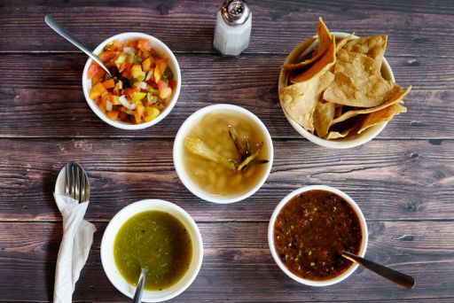 An overhead closeup shot of different types of sauces and chips on a wooden table