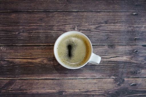 An overhead closeup shot of a white cup of coffee on a wooden table