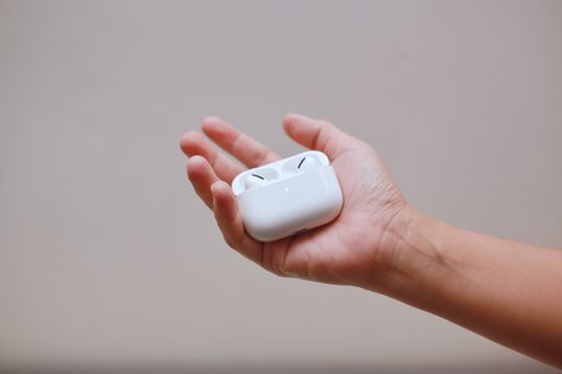 A hand holding Apple pro-Airpod case on a creme wall background.