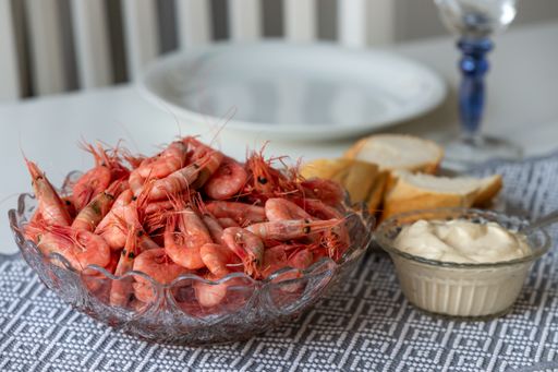 A soft focus a cooked shrimps in a glass bowl with garlic sauce and bread on a kitchen table