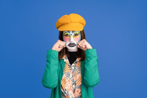 A Caucasian woman with carnival makeup pretending to cry isolated on a blue background