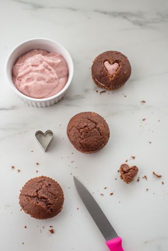 A vertical, top view of brown cupcakes with heart-shaped holes filled with cream