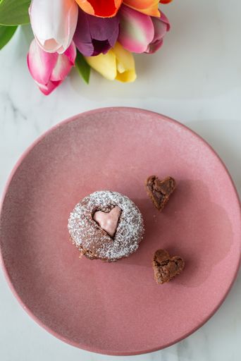 A vertical, top view of a brown cupcake and heart-shaped cakes on a pink plate