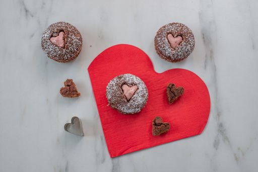 A top view of heart-shaped cupcakes on a red table mat