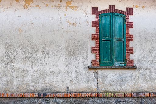 An exterior of an old medieval building with turquoise wooden window shutters on white weathered wall