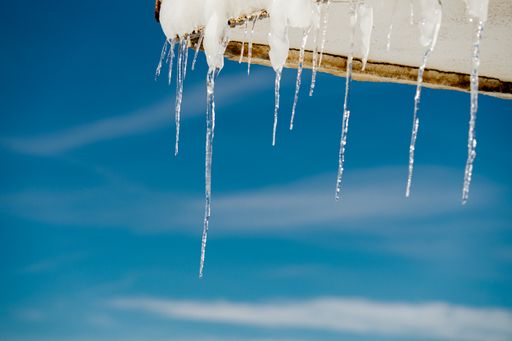 A closeup of icicles and snow on a roof of a building under a blue sky and sunlight