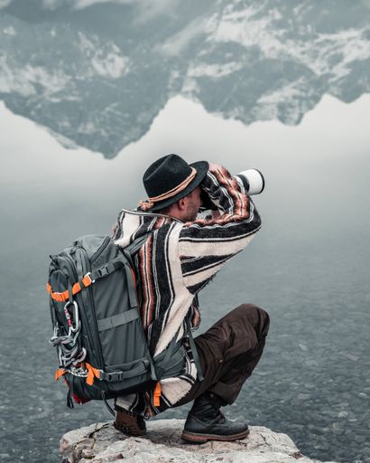 A guy photographing a lake reflecting the surrounding mountains on a coastal rock