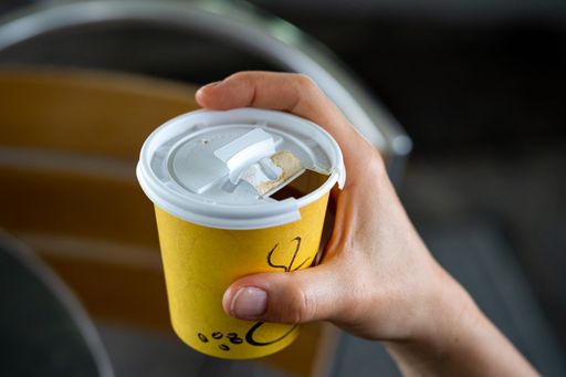 A close-up of a person holding a single-use paper cup of coffee.