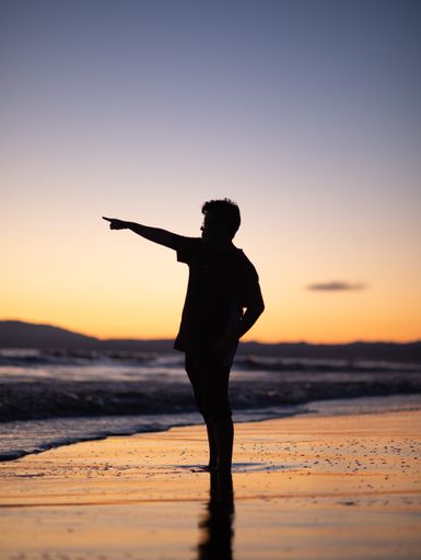 A vertical shot of a boy silhouette showing somewhere standing on a beach.