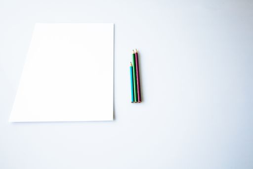 An overhead shot of coloring pencils near a white paper on a white surface