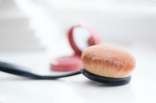 A closeup shot of a makeup brush neat a cosmetic compact mirror