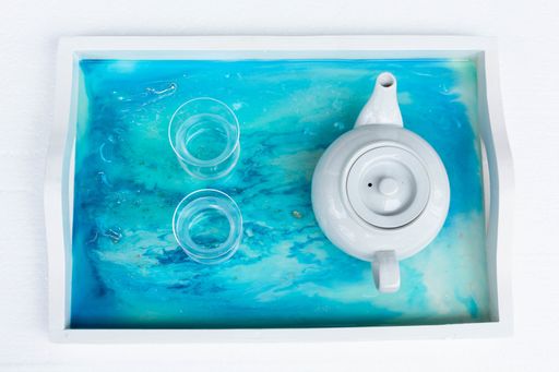 A high angle closeup shot of a teapot and cups on a blue tray with epoxy resin art
