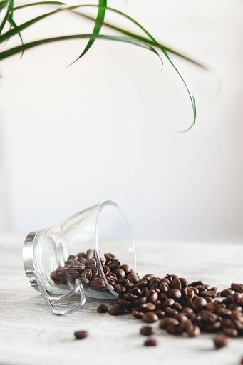 A vertical shot of a cup on the table with roasted coffee beans under the lights