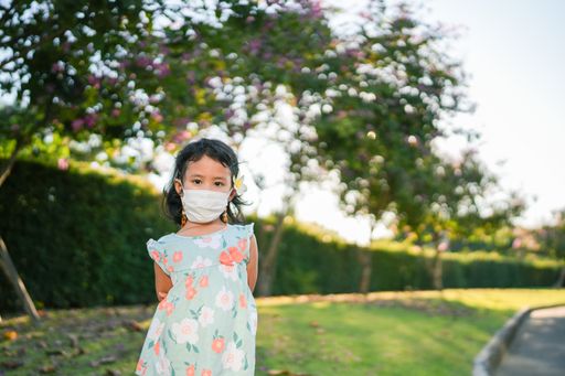 A shallow focus shot of a southeast asian child in a medical mask with flower behind ear in outdoor
