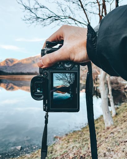 A man holding a camera taking a picture of reflection of water