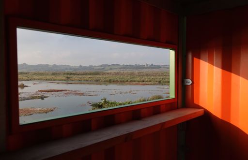 A beautiful scenic view of a nature reserve on a sunny day seen through the open window of a bird hide.