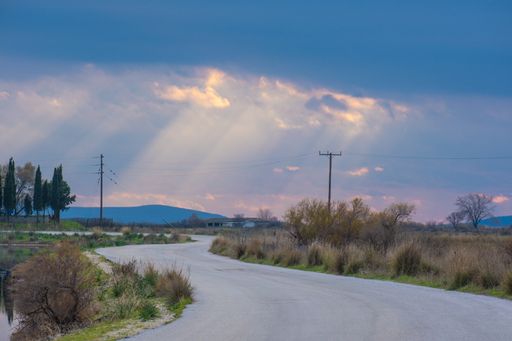 A twisty road under the sun rays through a cloudy sky