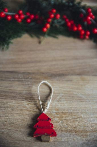 A closeup shot of a red pine tree hanging decor on a wooden table and red mistletoe in the background