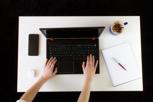 A high angle shot of a person working at a work desk with a laptop, a cup of coffee, mobile phone, notepad, and headphones - Covid-19 lockdown
