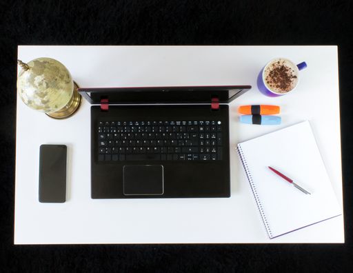A high angle shot of a work desk with a laptop, a cup of coffee, mobile phone, notepad, and headphones