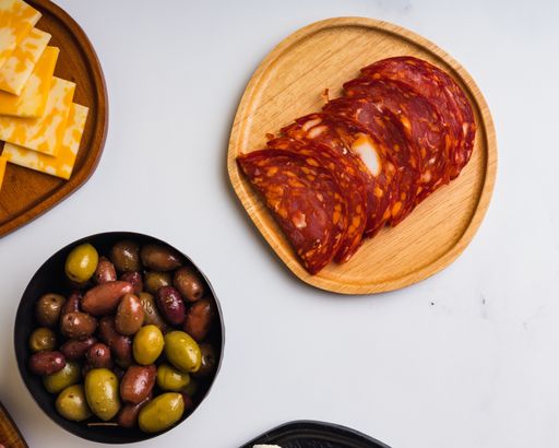 An overhead shot of cured meat, cheese, and olives on white marble surface