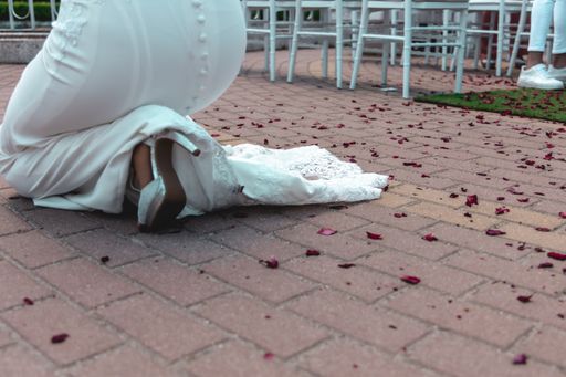 A selective focus shot of a bride kneeling on the brick ground with flower petals all around