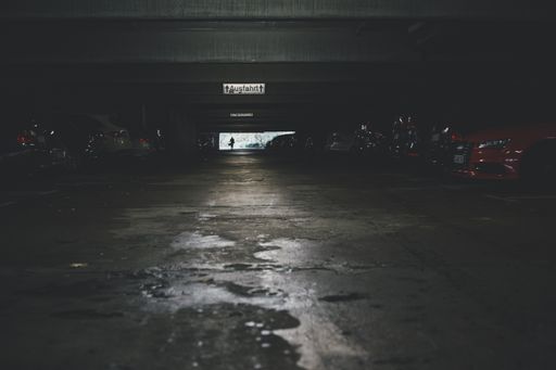 A low angle shot of an underground parking lot with a lot of cars and an exit sign