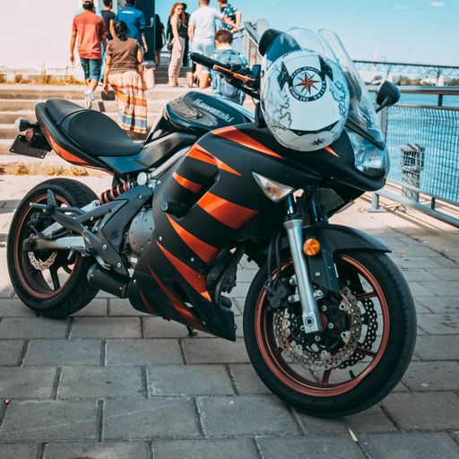 A shot of a black and orange motorbike with its helmet parked on the harborside