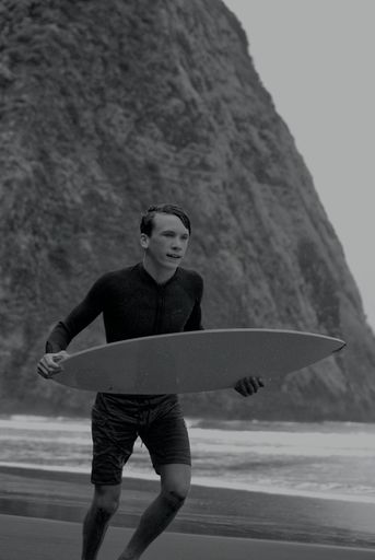 A vertical grayscale shot of a young surfer on a coast