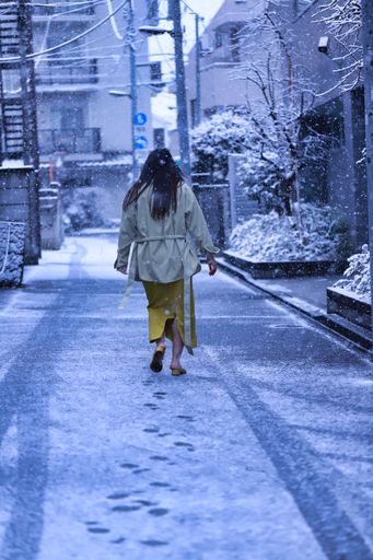 A vertical shot of the back view of the female walking in the snowy street