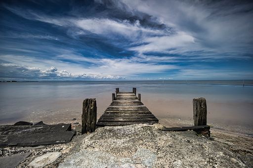 A mesmerizing scene of a long wooden pier to the water with a majestic cloudy blue sky on the horizon