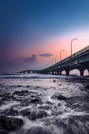 A vertical shot of a bright sunset sky over a bridge near the shore