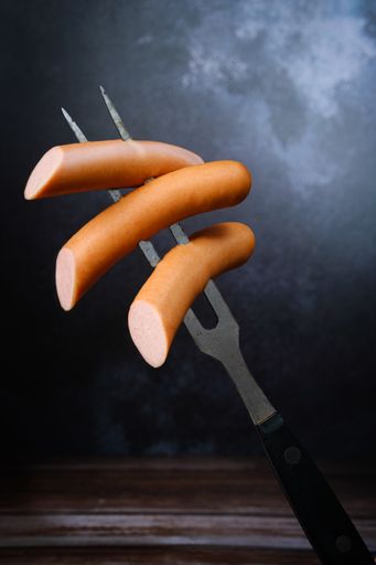 A vertical shot of a fork stabbing through sliced frankfurter sausages
