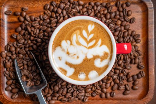A top view of hot tasty coffee on a wooden tray with coffee beans and a silver scoop