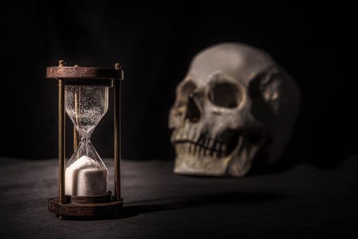 A closeup shot of a finished hourglass and a skull on a dark background- death concept