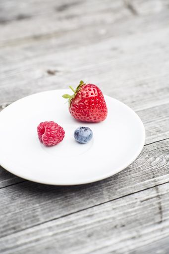 A white plate on a wooden table with sweet strawberry, raspberry, and blueberry