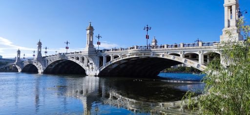 A scenic view of a bridge over a calm river under a clear sky
