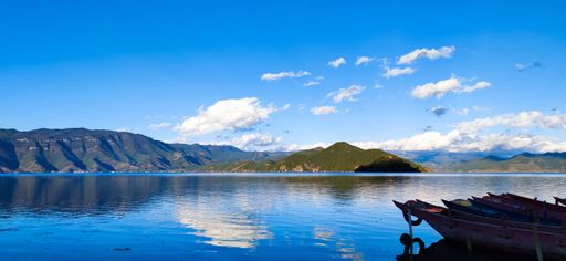 A mesmerizing panoramic scene of mountains reflecting on blue shiny water under a blue sky on a sunny day