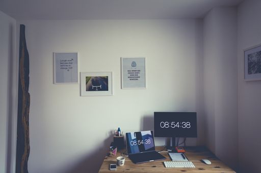 A high angle shot of a work desk with a computer, a laptop with time at 08:54:38 and posters with quotes hanging on the wall