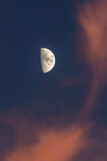 A vertical shot of a half moon at sunset with red clouds