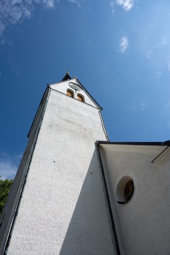 A low angle shot of a white tower of a church against a blue sky on a sunny day