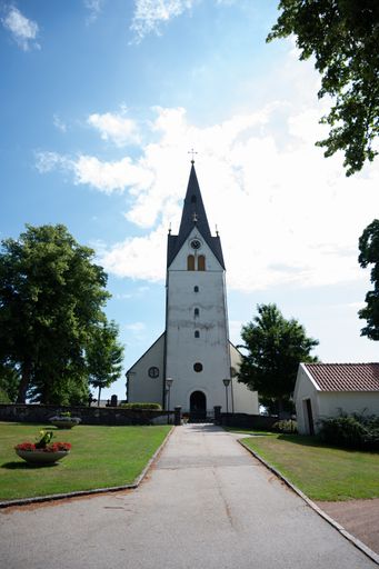 A vertical of a white tower of a church against a blue cloudy sky on a sunny day