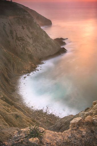 A beautiful, vertical shot of a beach surrounded by high rocks during the sunset, Lisbon, Portugal