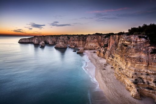 An aerial shot of a wavy beach surrounded by rocks and cliffs, Algarve, Portugal