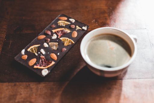 A cup of coffee and chocolate bar with nuts and dried fruit on a wooden table