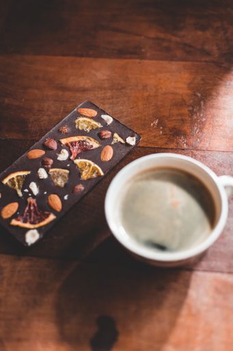 A vertical shot of a cup of coffee and chocolate bar with nuts and dried fruit on a wooden table